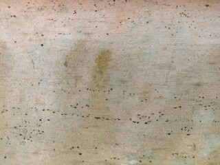 Textured Wall with Subtle Stains and Spots. A weathered beige and grey wall surface with small dark spots and faint discoloration, offering an abstract background