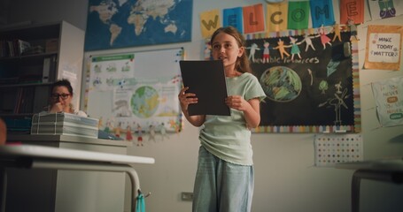 Primary School Girl with Notebook Speaking, Showcasing Knowledge of Ecology in Front of Classmates...