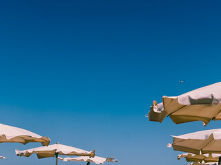 Fototapeta premium Tops of beach umbrellas with a plane flying in the distance, captured at Finikoudes Beach in Larnaca, Cyprus. Concept of summer vacation and seaside travel on the Mediterranean