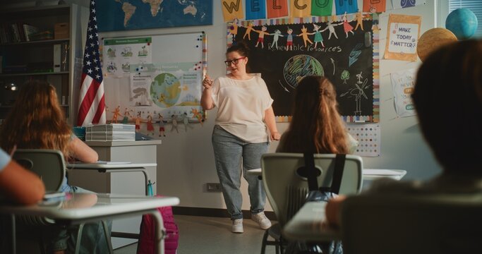 Female Teacher Conducting Lecture on Renewable Energy Resources to Elementary School Students. Smart Diverse Kids Sitting at Desks in Modern Colorful Classroom, Studying Ecology, Listening to Teacher. - Powered by Adobe