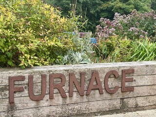 A rustic wooden planter overflows with lush greenery and vibrant flowers.  Rusted metal letters...