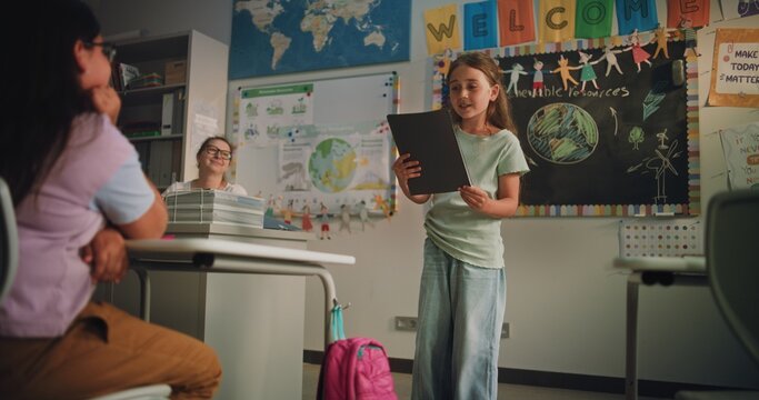 Primary School Girl with Notebook Speaking, Showcasing Knowledge of Ecology in Front of Classmates and Female Teacher. Smart Pupil Presenting Homework During Environmental Science Lesson. Dolly Shot.