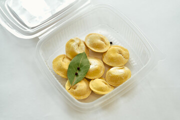 A Close-Up View of Handmade Dumplings Displayed in a Clear Container, Featuring a Preserved Bay Leaf and Spices for Culinary Presentation