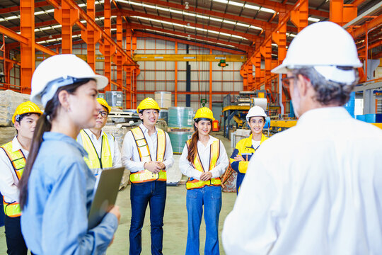 Senior engineer giving team briefing inside metal roofing factory, with workers listening attentively. Industrial meeting shows coordination and communication in manufacturing sector.