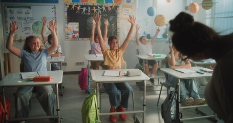 Female Teacher Conducting Funny Interactive Lesson to Primary School Children. Happy Young Boys and Girls Sitting at Desks, Raising Hands, Interacting with Teacher During Dynamic Classroom Activity.