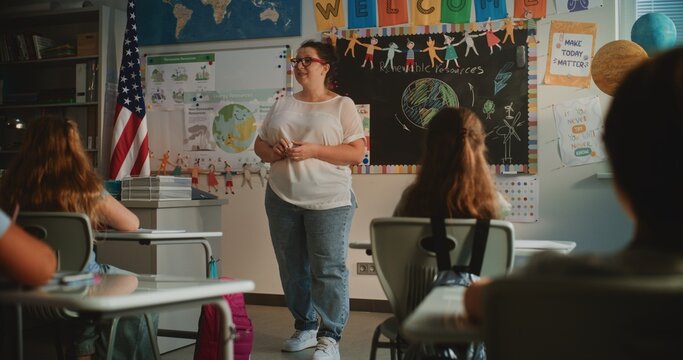 Female Teacher Conducting Lecture on Renewable Energy Resources to Elementary School Students. Smart Diverse Kids Sitting at Desks in Modern Colorful Classroom, Studying Ecology, Listening to Teacher. - Powered by Adobe