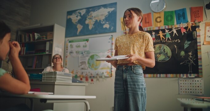 Primary School Girl Holding Notebook Speaking, Showcasing Knowledge of Ecology in Front of Classmates and Teacher. Smart Pupil Presenting Homework During Environmental Science Lesson. Dolly Shot.