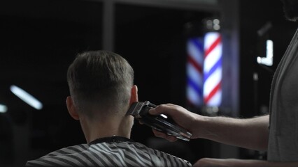 Skilled barber trimming client's hair with electric razor, creating precise contemporary hairstyle...