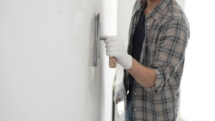 Unknown male construction worker wearing gloves and plaid shirt is using finishing trowel to...