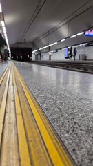 Underground metro platform in Bolhão station, Porto, Portugal. Captured from floor level, highlighting tactile safety lines and blurred commuters waiting in the distance. Urban rhythm and anticipation