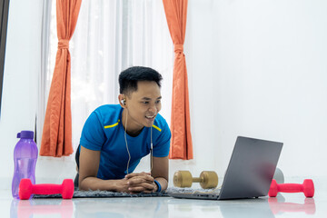 Asian man performing Plank exercise at home with dumbbells and a water bottle nearby. Wellness and Healthy lifestyle concept