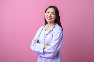 Asian female doctor in white coat and stethoscope smiling confidently with arms crossed, standing...