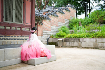 A Korean woman in her twenties wearing a charming pink hanbok sits in front of the traditional...