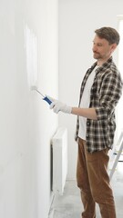 Professional house painter wearing gloves painting a white wall with a paint roller, working on a...