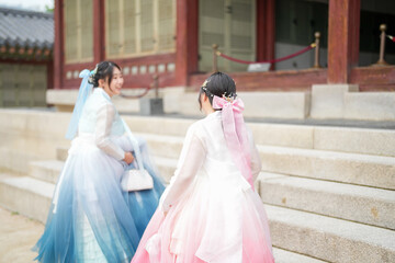 In Seoul in June 2025, two Korean women in their twenties wearing pink and sky-blue hanbok stand in...