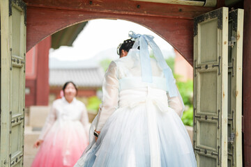 In Seoul in June 2025, two Korean women in their twenties wearing pink and sky-blue hanbok stand in...