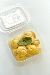 A Delicious Collection of Freshly Made Ravioli in a Clear Container Garnished with Bay Leaves and Peppercorns, Ready to Be Cooked and Enjoyed