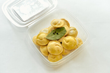 A Delicious Array of Freshly Prepared Dumplings Neatly Arranged in a Clear Plastic Container with Bay Leaves and Spices Ready for Cooking or Serving