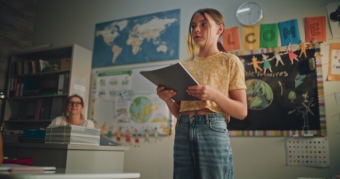 Primary School Girl Holding Notebook Speaking, Showcasing Knowledge of Ecology in Front of Classmates and Teacher. Smart Pupil Presenting Homework During Environmental Science Lesson. Dolly Shot.