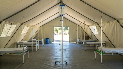 Interior of a temporary field hospital or medical tent, equipped with multiple empty cots or beds, suggesting readiness for emergency response, disaster relief, or humanitarian aid