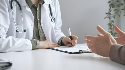 Doctor woman listening to male patient health concerns and writing a prescription on a clipboard...
