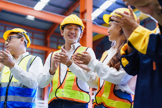 Diverse factory employees wearing protective gear celebrating together at indoor warehouse location. Emotion of unity and recognition boosts workplace morale.