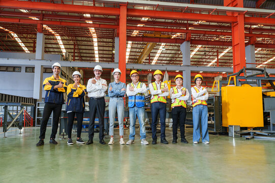 Diverse team of factory workers, engineers, and office staff pose confidently inside modern steel roofing sheet production plant. Their stance reflects unity, pride, and industrial teamwork