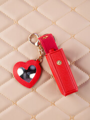 Close-up of a red leather lipstick case with a heart-shaped mirror, elegantly placed on a  beige...
