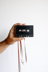 Male hand holding vintage black audio cassette tape with loose tape unraveled