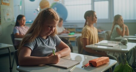Focus on Elementary School Girl Writing in School Notebook During Geography Lesson in Modern...