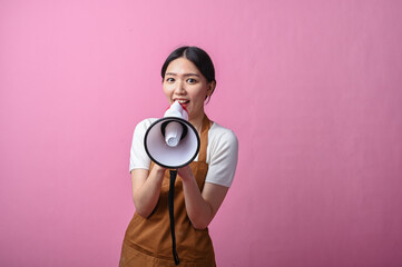 Asian woman in brown apron holding a white and red megaphone, appearing to speak confidently,...