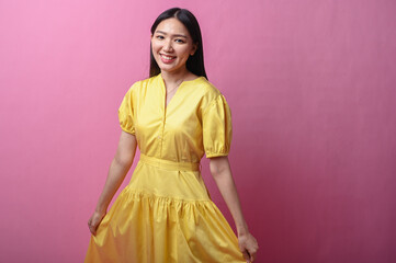 Asian woman with long black hair wearing a bright yellow dress smiling and holding the hem of her...