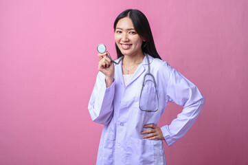 Asian female doctor smiling while holding stethoscope chest piece near her face, wearing white coat...