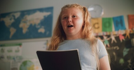 Primary School Girl with Notebook Speaking, Showcasing Knowledge of Geography in Front of Classroom. Smart Pupil Presenting Homework During Environmental Science or Ecology Lesson. Close Up Shot.
