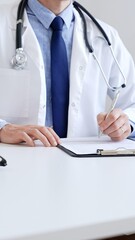 Unreckognisable doctor man writing a prescription and filling out medical records on a clipboard in...
