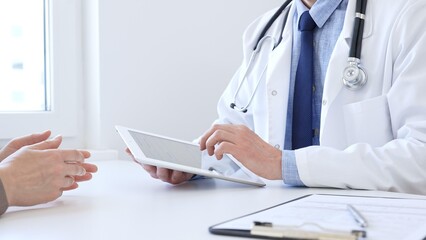 Close-up of doctor man showing information on tablet to patient woman during medical visit,...