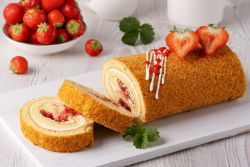 Delicious strawberry roll cake served on a wooden board with fresh strawberries in a white bowl in the background