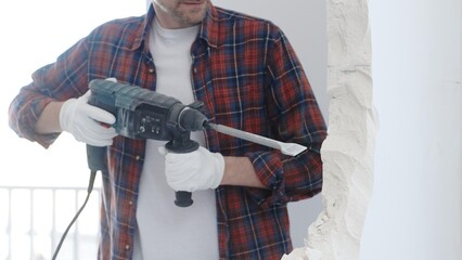 Male construction worker wearing red checkered shirt and protective white gloves is demolishing...