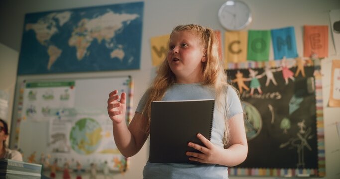 Primary School Girl with Notebook Speaking, Showcasing Knowledge of Geography in Front of Classmates and Teacher. Smart Pupil Presenting Homework During Environmental Science Lesson. Dolly Shot.