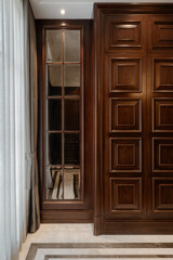 Classic interior with dark wood paneled walls and a mirrored window cabinet. Elegant curtains and marble flooring complete the traditional luxury look.