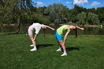 Two girls in sportswear doing stretching exercises in the park.