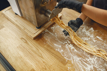 A skilled chef expertly using a pasta machine to create fresh noodles in a beautifully styled...