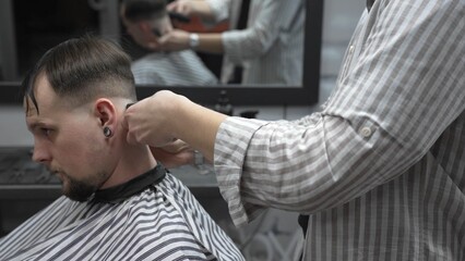 Professional barber trimming customer's hair with electric clipper, focusing on precise nape grooming within contemporary barbershop interior design