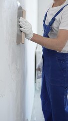 Male construction worker wearing protective gloves and blue construction coveralls, spreading...