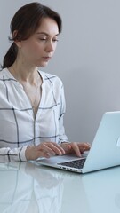 Professional businesswoman working on laptop, sitting at glass desk in bright contemporary...