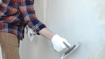 Unknown male construction worker wearing protective gloves smoothing plaster on interior wall...