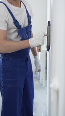 Professional construction worker wearing blue work overall is using a finishing trowel to carefully...