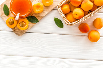 Summer preserves. Apricot jam in jar near fresh fruits on white wooden background top view frame...