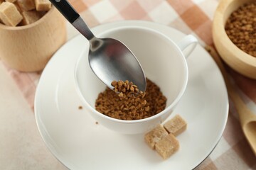 Putting instant coffee into cup at light table, closeup