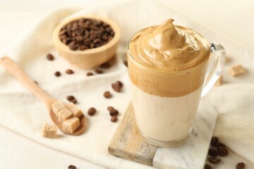 Delicious dalgona coffee in glass cup, beans and brown sugar on light table, closeup
